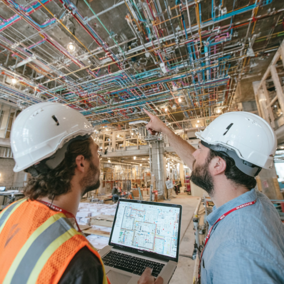 An engineer and architect on a commercial construction site, using laptops and tablets to check BIM models.